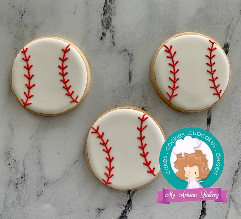 Pu&ograve; includere: Tre biscotti al burro a tema baseball, bianchi e rossi, con dettagli di cuciture rosse. I biscotti sono su uno sfondo grigio.