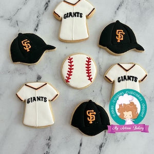 Pu&ograve; includere: Sei biscotti di zucchero decorati a tema baseball. I biscotti sono decorati con maglie da baseball, cappellini da baseball e una palla da baseball. Le maglie e i cappellini sono decorati con il logo dei San Francisco Giants e la parola "Giants".