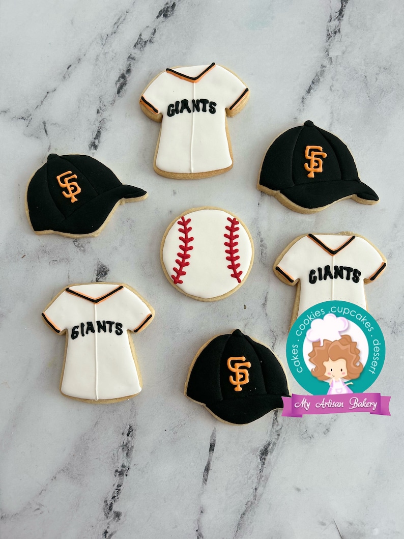 Pu&ograve; includere: Sei biscotti di zucchero decorati a tema baseball. I biscotti sono decorati con maglie da baseball, cappellini da baseball e una palla da baseball. Le maglie e i cappellini sono decorati con il logo dei San Francisco Giants e la parola "Giants".