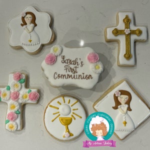 May include: Set of six decorated sugar cookies for a First Communion celebration. The cookies feature a girl in a white dress, a cross with pink flowers, a chalice with a sunburst, and a banner that says "Sarah's First Communion".