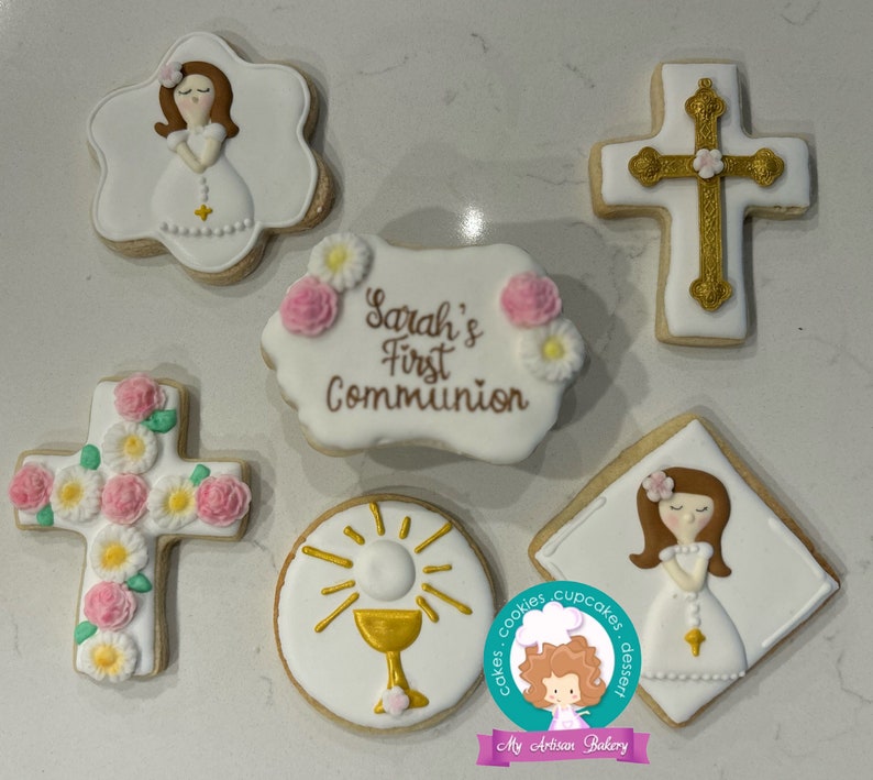 May include: Set of six decorated sugar cookies for a First Communion celebration. The cookies feature a girl in a white dress, a cross with pink flowers, a chalice with a sunburst, and a banner that says "Sarah's First Communion".