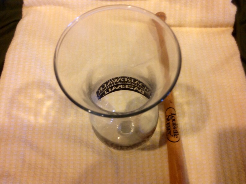 May include: A clear glass with the word "BASEBALL" printed on it, and a Louisville Slugger wooden baseball bat.
