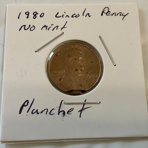 May include: A 1980 Lincoln penny with a planchet error. The coin is in a plastic coin holder with the text "1980 Lincoln Penny no mint Planchet" written on it.