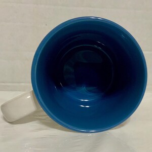 May include: A ceramic mug with a white handle and a deep blue interior. The mug's interior is a glossy, solid blue, contrasting with the white handle. The mug is empty and viewed from above.