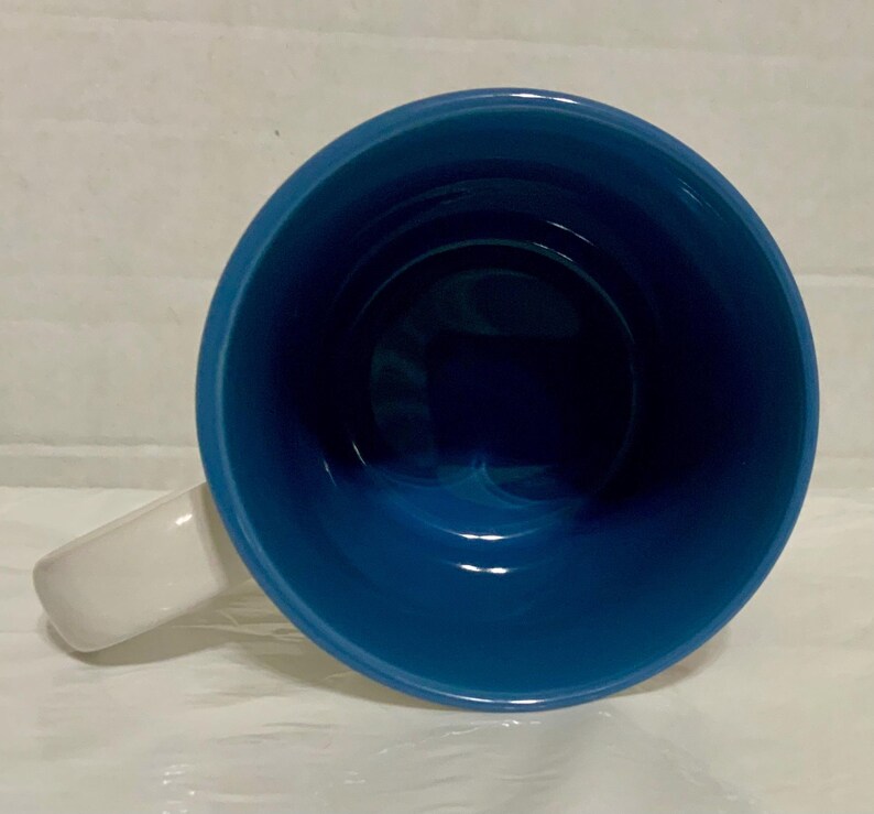 May include: A ceramic mug with a white handle and a deep blue interior. The mug's interior is a glossy, solid blue, contrasting with the white handle. The mug is empty and viewed from above.