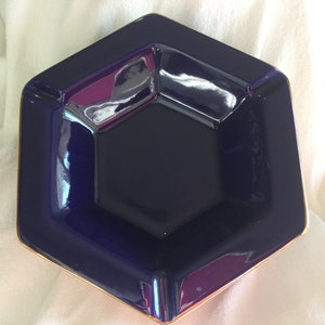 May include: A hexagonal blue ceramic ashtray with a gold rim. The ashtray is made of a glossy material and has a deep well.