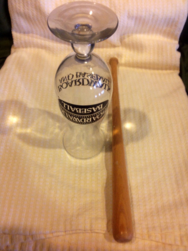 May include: A clear glass with a black and white label that reads "Boardwalk Baseball" and a wooden baseball bat.