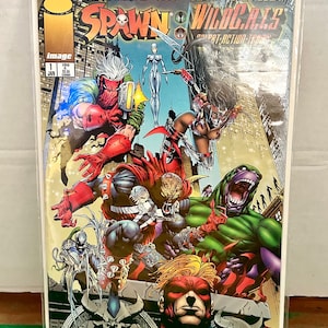 May include: Comic book cover featuring Spawn and WildC.A.T.S. characters in a fight scene. The cover is red, green, blue, and black with the title "Spawn/WildC.A.T.S.  " and "Devil Day" in large letters.