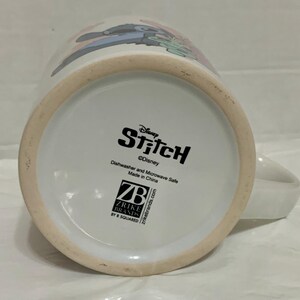 May include: White ceramic mug featuring the Disney character Stitch. The mug has a handle and a design of Stitch on the side. The bottom of the mug has the Disney Stitch logo and text indicating it is dishwasher and microwave safe.