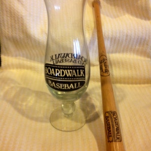 May include: A clear glass with a black and white logo that says "Boardwalk Baseball" and a wooden baseball bat with a black and white logo that says "Boardwalk Baseball".