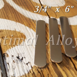 Pu&ograve; includere: Tre strisce di metallo argentato, ciascuna di 1,9 cm per 15,2 cm, sono disposte una accanto all'altra su una superficie di legno. Il legno presenta un disegno dipinto di bianco e il testo "Optimal Alloys" &egrave; visibile sullo sfondo.