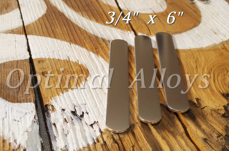 Pu&ograve; includere: Tre strisce di metallo argentato, ciascuna di 1,9 cm per 15,2 cm, sono disposte una accanto all'altra su una superficie di legno. Il legno presenta un disegno dipinto di bianco e il testo "Optimal Alloys" &egrave; visibile sullo sfondo.