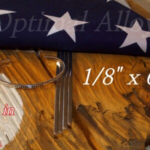 May include: Four silver metal rods, 1/8 inch by 6 inches, with a silver metal bracelet that says "Optimal Alloys" on it. The rods and bracelet are on a wooden surface with a folded American flag in the background. The text "Made in the USA" is visible in the lower left corner.