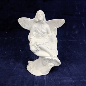 May include: White ceramic fairy figurine sitting on a mushroom. The fairy has wings and is holding a flower.