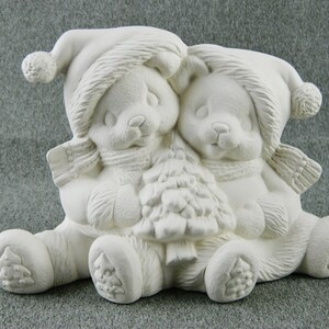 May include: A ceramic figurine featuring two bear cubs wearing winter hats and scarves, hugging a small Christmas tree. The bears are in a sitting position, with detailed textures and a matte finish. The figurine is unpainted and ready for customization.