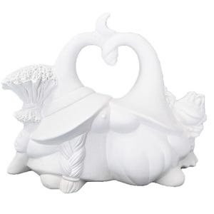 May include: A white ceramic sculpture of two witch-like figures facing each other, forming a heart shape. Each figure wears a hat and has a long braid. One figure holds a broom. The sculpture is a decorative item.