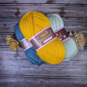 May include: Three skeins of Stylecraft Special double knit yarn in mustard yellow, teal blue, and pale mint green. Each skein features a brown paper label with the text Stylecraft Special double knit printed in white, along with two beige flowers.