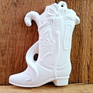 May include: White ceramic boot ornament with a candy cane and a gift inside. The boot has a detailed design and a hole for hanging.