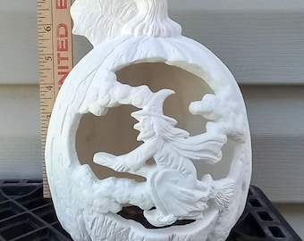 May include: A white ceramic pumpkin with a carved witch on a broomstick design. The pumpkin has a stem and leaf detail at the top. The witch is flying through clouds, creating a Halloween theme.