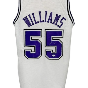May include: White basketball jersey with the name "WILLIAMS" in purple arched across the back, and the number "55" in purple with a black outline. The jersey has black and white trim around the neck and armholes.