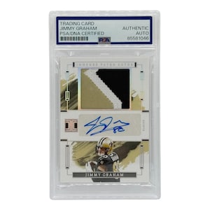 May include: A trading card featuring Jimmy Graham, authenticated by PSA/DNA. The card includes a patch of fabric with black, gold, and white colors, along with an autograph. The card is encased in a protective holder.