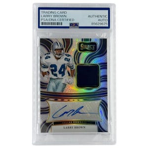 May include: A trading card featuring Larry Brown of the Dallas Cowboys, with the number 24 on his jersey. The card is encased in a protective holder and includes an autograph and a piece of the player's jersey. The card is certified by PSA/DNA.
