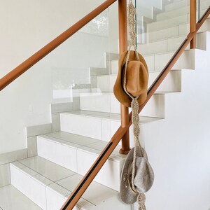 May include: Two brown and beige cowboy hats hanging on a wooden railing with a macrame rope.