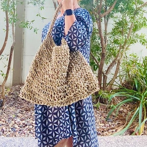 May include: A woman is wearing a blue and white patterned dress and carrying a large, light brown, crocheted tote bag.