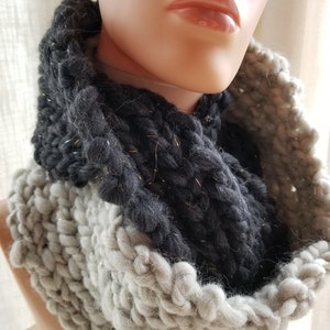 May include: A chunky knit infinity scarf in shades of gray and black, with a touch of gold sparkle. The scarf is displayed on a mannequin, showcasing its thick, textured weave. This cozy accessory is perfect for cold weather.