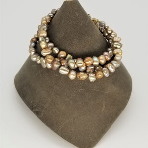 May include: A multi-strand pearl bracelet with a mix of beige, brown, and grey pearls. The pearls are irregular in shape and size, giving the bracelet a unique and natural look.