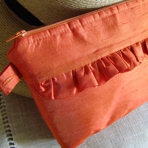 Bolso de mano tipo pulsera en tejido de color naranja mango que imita la seda, con un delicado volante en la parte delantera. ¡Muy elegante! Ideal como neceser de maquillaje.