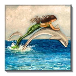 May include: A painting of a mermaid riding a dolphin in the ocean. The mermaid has long brown hair and a green tail. The dolphin is gray and is jumping out of the blue water. The sky is a light blue with white clouds.