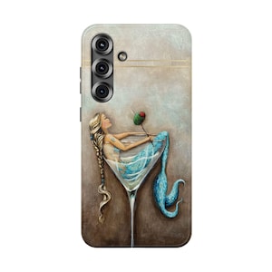 May include: A phone case featuring a mermaid relaxing in a martini glass with an olive. The mermaid has long blonde hair and is wearing a blue outfit. The background is a textured, neutral color.
