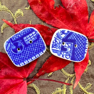 May include: Two blue and white ceramic buttons with a traditional Chinese design. The buttons are rectangular and have two holes each.