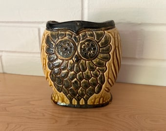 May include: A ceramic owl planter with a brown and tan glaze. The owl's eyes are black and the planter has a textured surface.