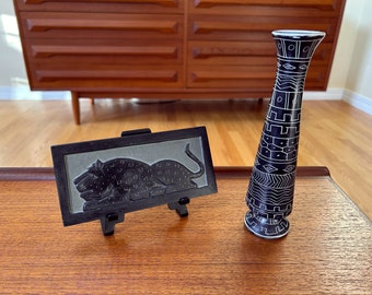 May include: A black and white stone vase with geometric patterns and a black stone plaque with a carved image of a leopard.