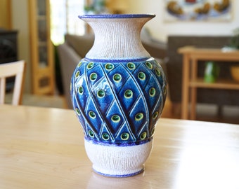 May include: A blue and white ceramic vase with a textured surface and green accents. The vase has a diamond pattern and is decorated with small, round, green and blue dots.