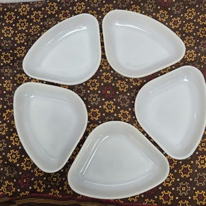 May include: Five white, organically shaped serving dishes. The dishes are arranged on a brown patterned fabric with a decorative border. The dishes have a smooth, glossy finish and a shallow depth, suitable for serving appetizers or small portions.