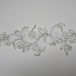 Peut inclure: Garniture en dentelle florale argentée avec un motif délicat de fleurs et de feuilles. La garniture est parfaite pour ajouter une touche d'élégance à tout projet.