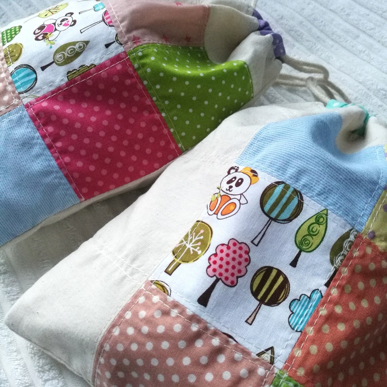 May include: Two fabric bags with patchwork designs. The first bag is made of pink, blue, green, and white fabric with a small panda bear design. The second bag is made of white, blue, and brown fabric with a panda bear design and a tree design.