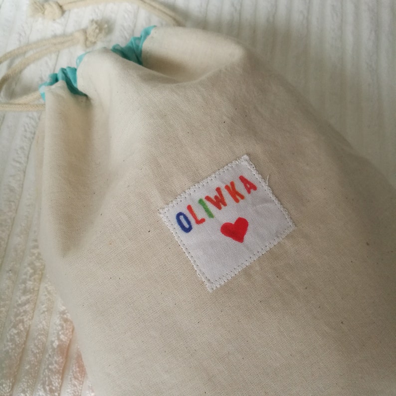 May include: A white canvas drawstring bag with a colourful embroidered patch that says "OLIWKA" with a red heart.
