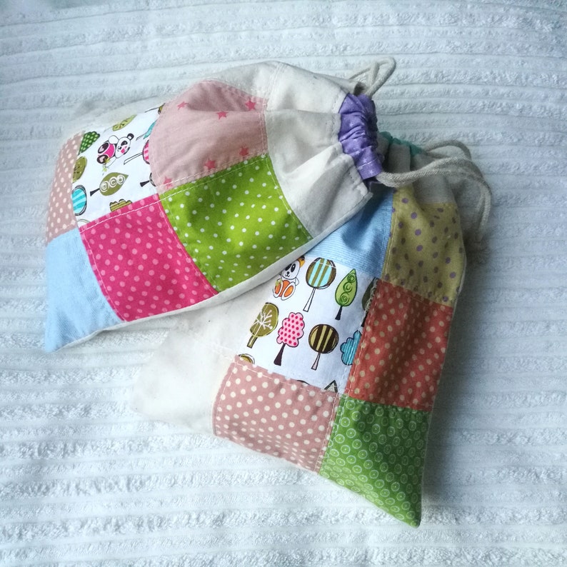 May include: Two patchwork fabric drawstring bags with different patterns. One bag is light blue, pink, green, and white with a panda bear design. The other bag is white, light blue, green, pink, and brown with a tree design.