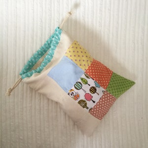 May include: A white drawstring bag with a patchwork design. The patches are made of different fabrics with various patterns, including polka dots, stripes, and a panda bear design.