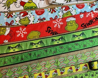 May include: A set of seven colorful dog collars featuring a Grinch theme. The collars are made of different materials, including fabric, ribbon, and webbing. The Grinch's face, along with other Christmas-themed designs, are printed on the collars. The collars are in various shades of green, red, and white.
