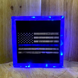 May include: A blue light-up glass block with a black and white American flag with a blue line etched into it.
