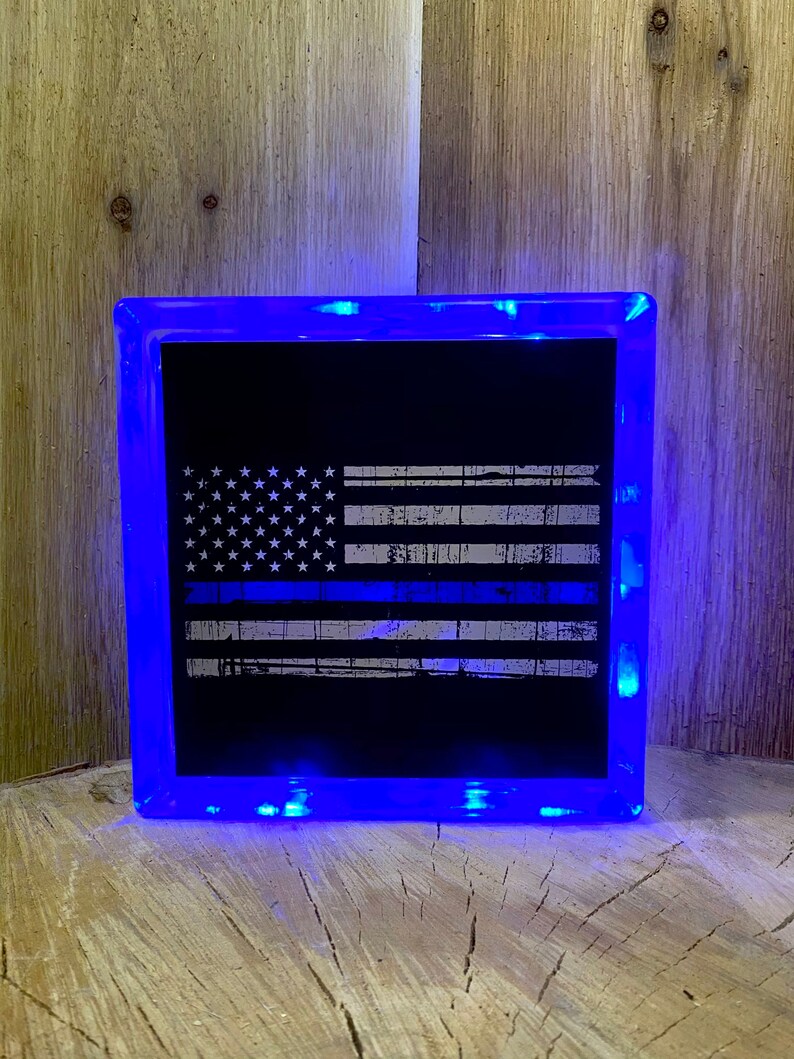 May include: A blue light-up glass block with a black and white American flag with a blue line etched into it.