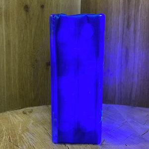 May include: A blue glass block with a smooth, polished surface. The block is illuminated from within, creating a bright blue glow.