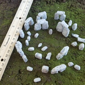 May include: A miniature Stonehenge model made of grey and white stones. The model is made of small, individual stones that are arranged in a circle. The stones are about 2.5 cm tall and are arranged in a circle.