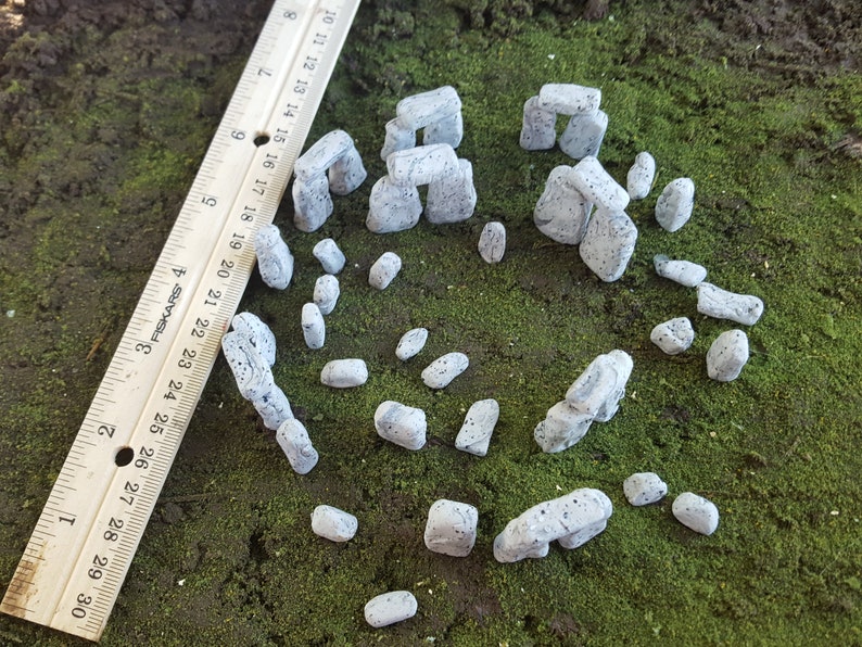 May include: A miniature Stonehenge model made of grey and white stones. The model is made of small, individual stones that are arranged in a circle. The stones are about 2.5 cm tall and are arranged in a circle.