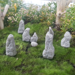 Może przedstawiać: Miniaturowy ogr&oacute;d kamienny z siedmioma szarymi kamiennymi figurami ułożonymi w k&oacute;łko na ł&oacute;żku z zielonego mchu.